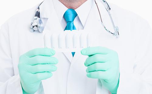 Руки врача в перчатках держат медицинские свечи
