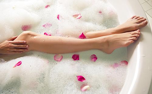 Девичьи ноги в пенистой ванне с розовыми лепестками
