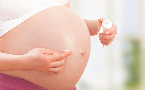 Беременная женщина наносит крем на живот