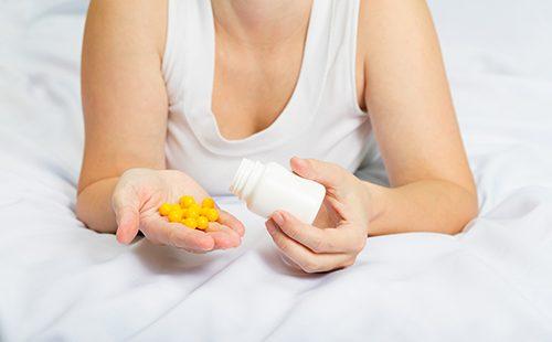 Женщина в постели держит жёлтые таблетки